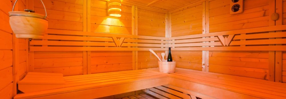 Innenansicht einer Holzsauna mit Bänken und Saunazubehör.